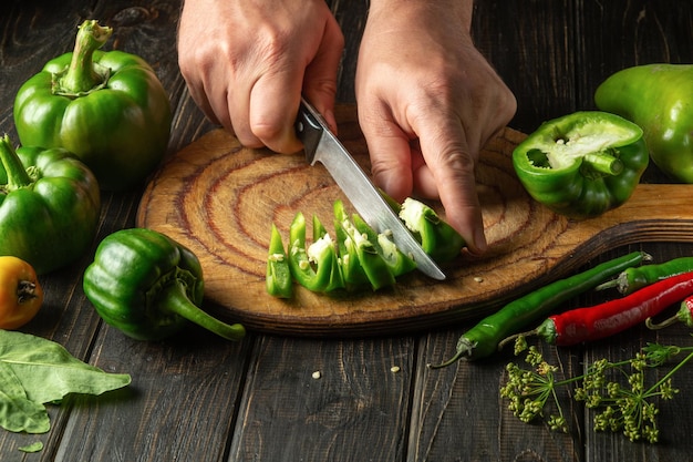 Slicing green fresh peppers on a cutting board by the hands of a chef