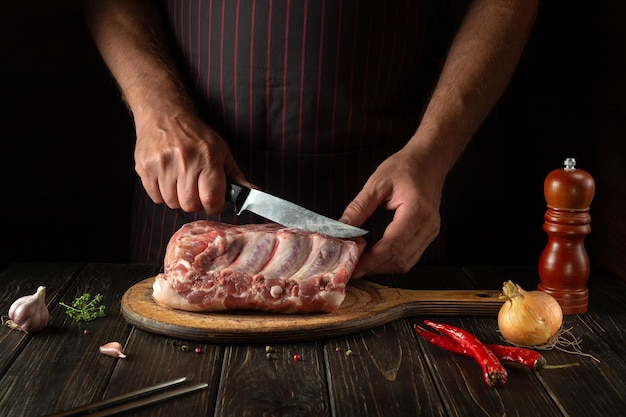 Slicing raw ribs with butcher or cook hands on kitchen cutting board Barbecue grill Idea for a restaurant or hotel menu on a dark background