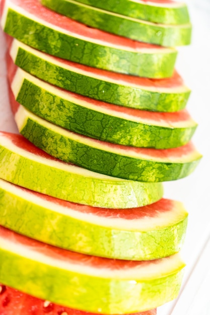 Slicing red seedless watermelon on a white cutting board.