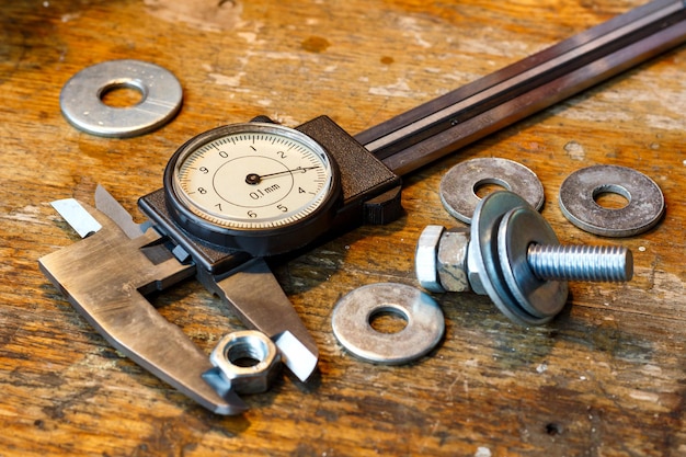 Slide caliper with round scale and bolt with nuts on the workbench in workshop