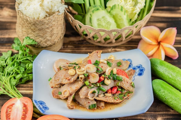 Slide grilled pork salad with sticky rice and many vegetable on wooden table background.