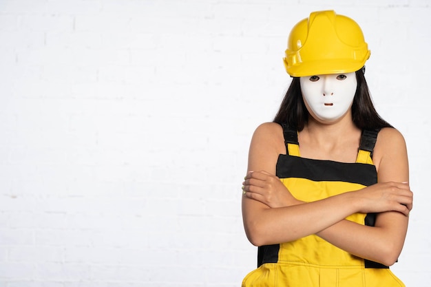 Slightly hunched and with folded arms a young construction worker stands and waits for a line of white bricks Stubborn employee