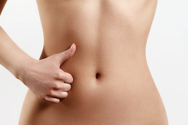 Slim, athletic waist of a young woman. The hand in the foreground shows a finger up gesture. the concept of female beauty and health, nutrition and diet, beautiful figure