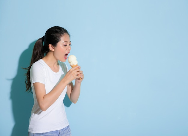 slim beauty female model standing on blue wall background eating delicious ice cream forget having sensitive tooth disease problem.