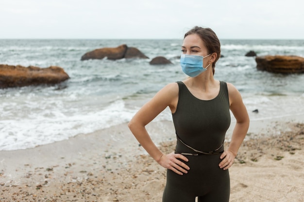 Slim fit woman in medical mask on the beach Sports during the pandemic