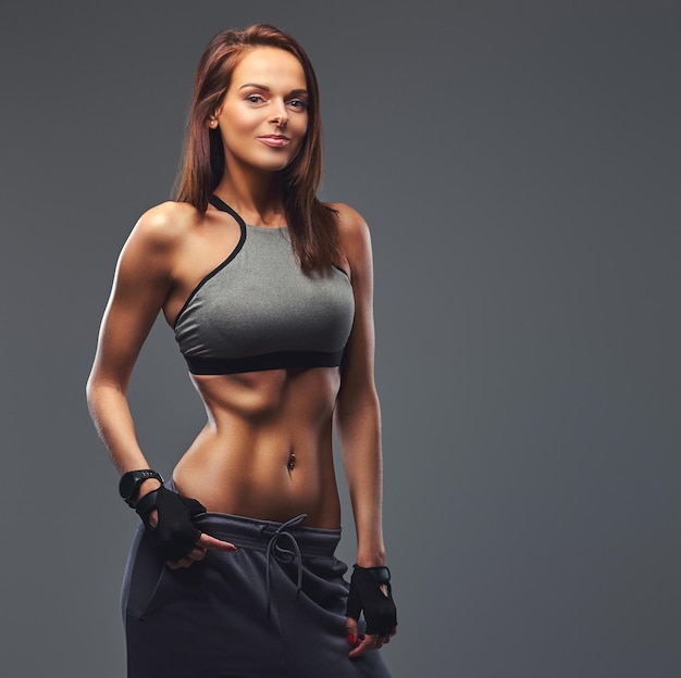 Slim fitness brunette woman in a gray sportswear posing in a studio. Isolated on a gray background.