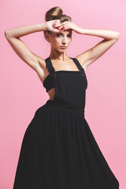 Slim girl on in a black top on a pink studio background. Slim model posing in the studio