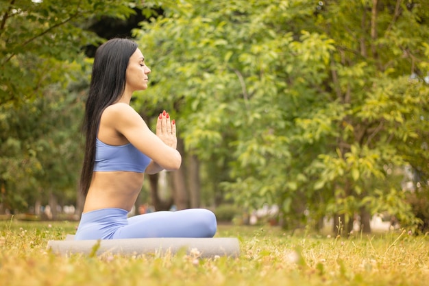 Slim girl meditating sitting in a lotus pose with closed eyes on the lawn in a park