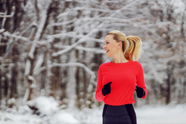 Slim sportswoman running in woods at snowy winter day. Cardio exercises, nature fitness, winter fitness