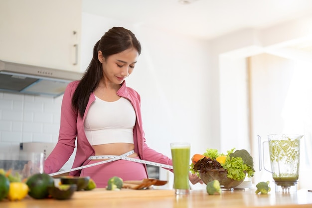 A slim woman in sportswear measured her waist with a measuring tape while cooking in the kitchen