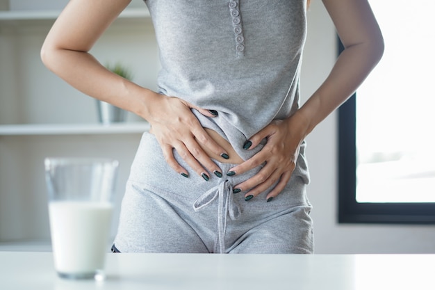 Slim woman with stomach ache and pain holding a glass of milk.