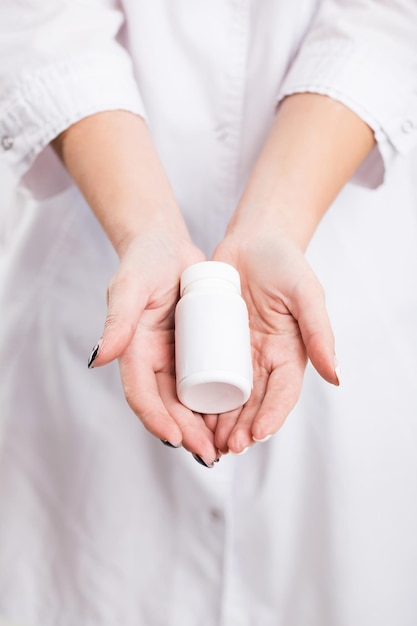 Slim young girl in white doctors smock holds bottle with drugs indoor isolated shot