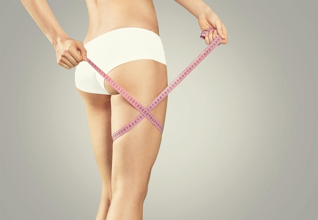 Slim young woman measuring her thin leg with a tape measure, close up