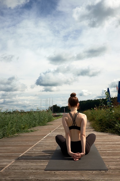 Slim young woman practicing yoga on the wooden pier near lake.