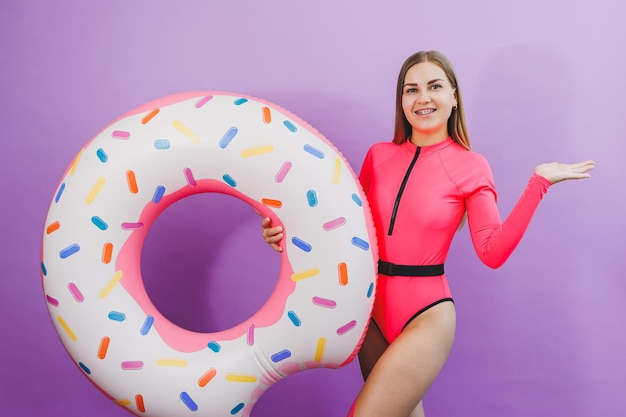 Slim young woman in a stylish pink swimsuit with a donut inflatable ring on a plain background