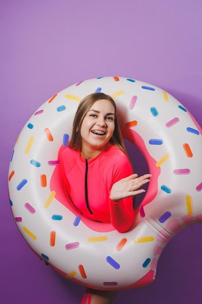 Slim young woman in a stylish pink swimsuit with a donut inflatable ring on a plain background