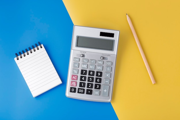 Sliver calculator on yellow and blue background with notepad and pencil