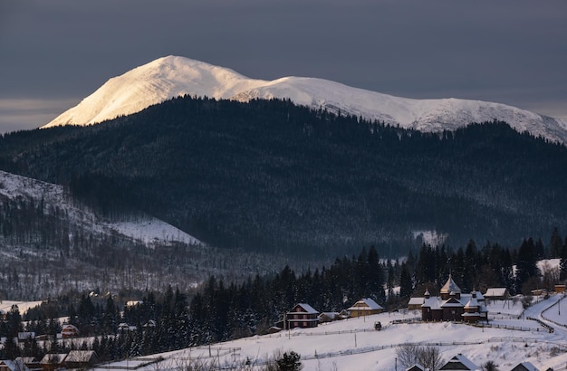 Small alpine village and winter snowy mountains in first sunrise sunlight around Voronenko Carpathian Ukraine