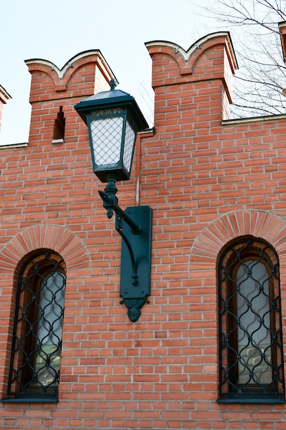 Small arched windows with metal bars in a red brick wall Beautiful lantern on the fortress wall