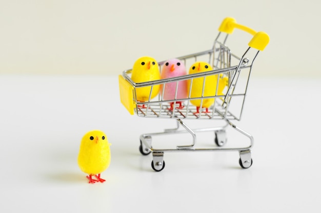 Small baby chicken toys of yellow and pink color in a shopping cart and one toy standing