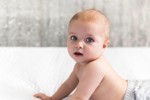 small baby of nine months is lying on his stomach leaning on his hands. child learns to crawl Lying on the bed is a copy space