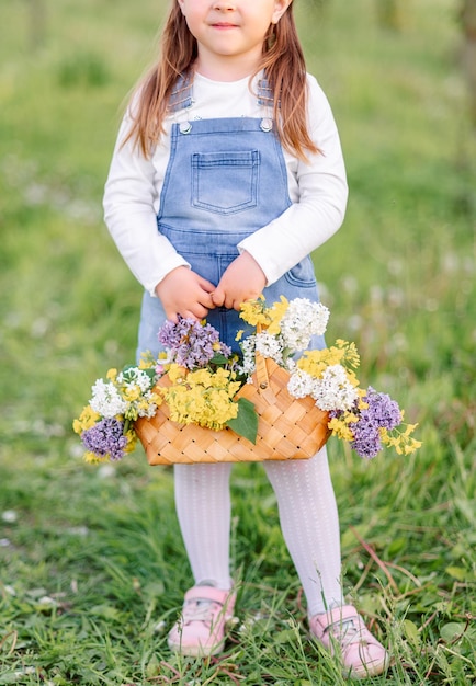 Small basket handbag with yellow flowers and lilacs in the hands of a girl