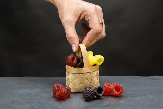 A small basket with handmade soap in the form of bright berries in a womans hand on a gray background