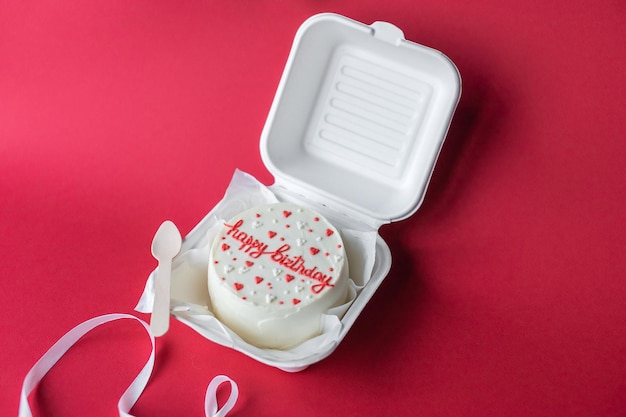 A small bento cake with lettering and hearts in a box with a wooden spoon Red background