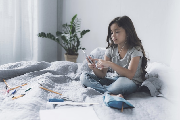 A small black-haired girl sits on a bed in white 