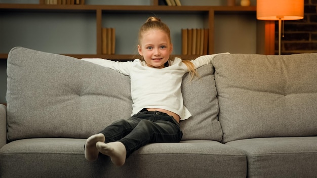 Small blonde school toddler child active kid falling down on comfortable sofa cozy couch for daytime