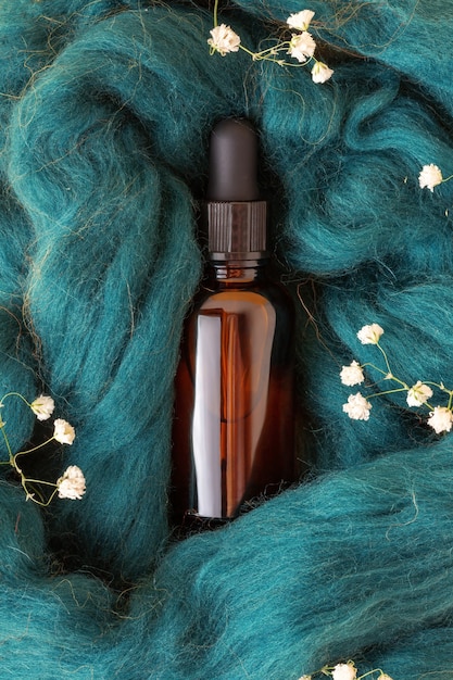 Small bottle with essential oil or serum on blue wool with gypsophila, closeup. Brown glass vial with liquid innovation cosmetics.