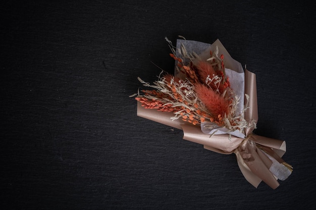 Small bouquet of dried flowers on a black background in terracotta colors, incredible art