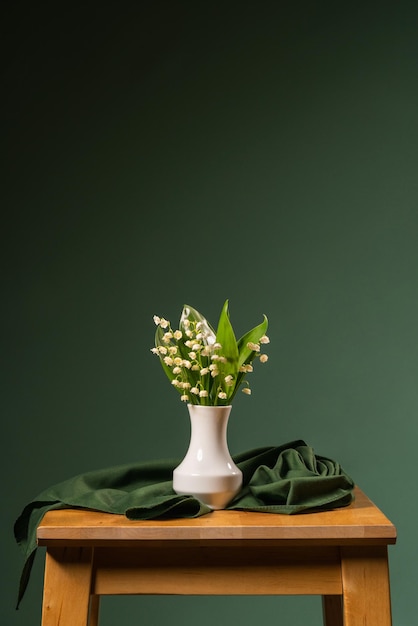 A small bouquet of lilies of the valley in a white vase green shawl green background still lif