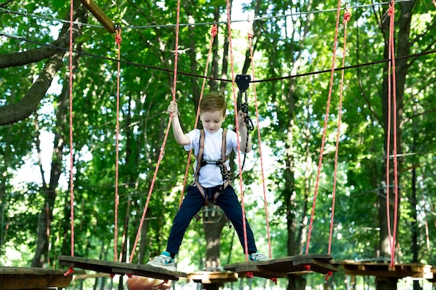 Small boy in climbing gear is walking along a rope road in an adventure