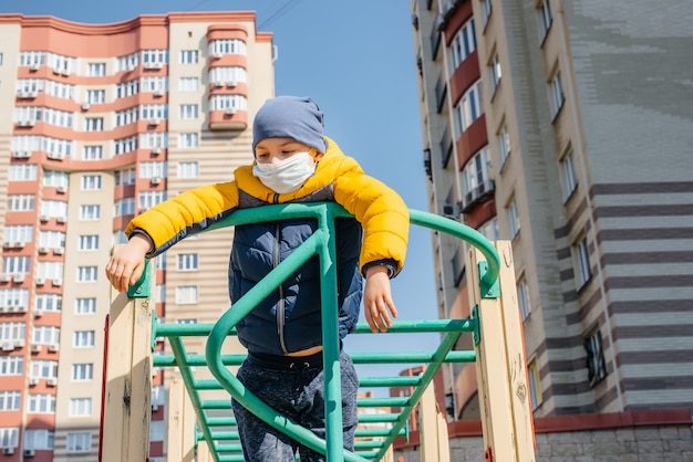 A small boy in a mask walks on the Playground during the quarantine. Stay at home.