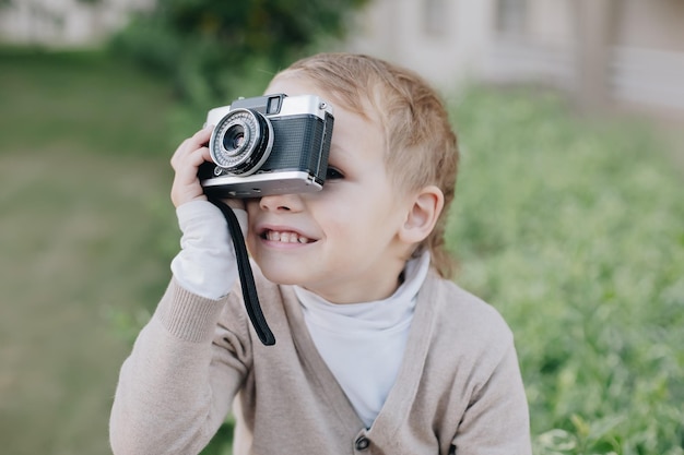 Small boy photographer smile with analogue film retro vintage photo camera outdoors