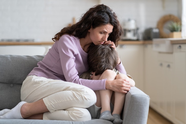 Small boy receive mother love protection and support mom cuddling son offended child cry on sofa