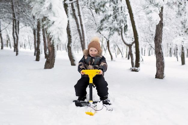 Small boy sits on a sledge snowcat in a snowcovered forest