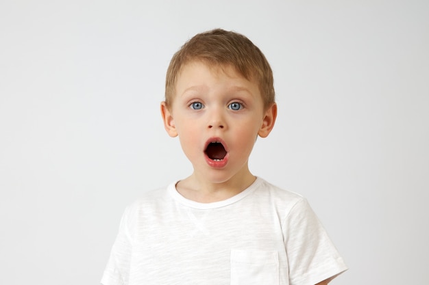 Small boy with blue eyes opened his mouth in surprise against a white background