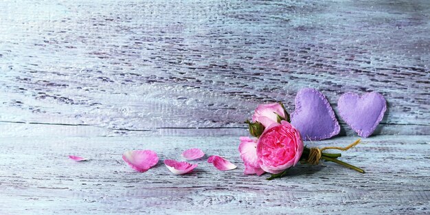 Small bunch of fresh roses and a couple of hearts on a wooden surface