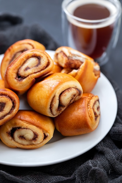 Small buns with cinnamon on white plate and cup of coffee on ceramic table