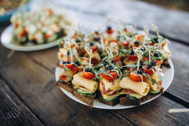 Small burgers with meat, salads cheese and tomatoes on wooden plate during summer barbecue party outdoors.