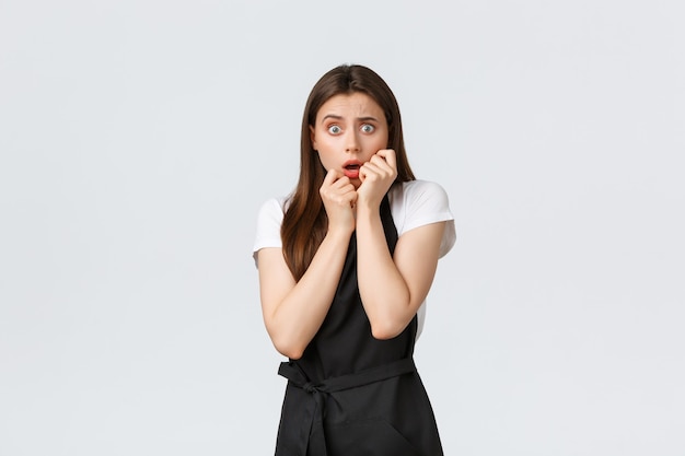 Small business, employees and coffee shop concept. Scared and insecure, troubled saleswoman in black apron, shivering from shock. Frightened barista staring terrified