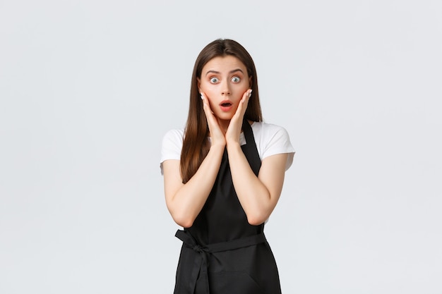 Small business, employees and coffee shop concept. Surprised and shocked saleswoman in grocery store gasping, looking surprised and impressed. Cafe worker standing astonished