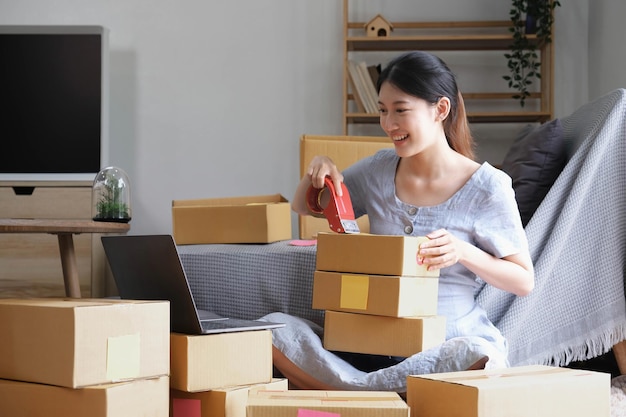 Small business entrepreneur SME asian young womangirl owner packing product checking parcel for delivery to customer using scotch tape to seal the box working at home Merchant online e commerce