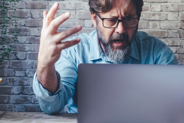 Small business freelance businessman shouting angry at the laptop in video call One male adult people doing business online and managing problems Exhausted worker in front of a computer shout angry