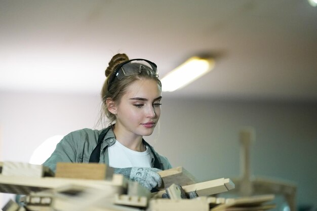 Small business of a young woman Beautiful young woman worker in a furniture workroom measuring wood