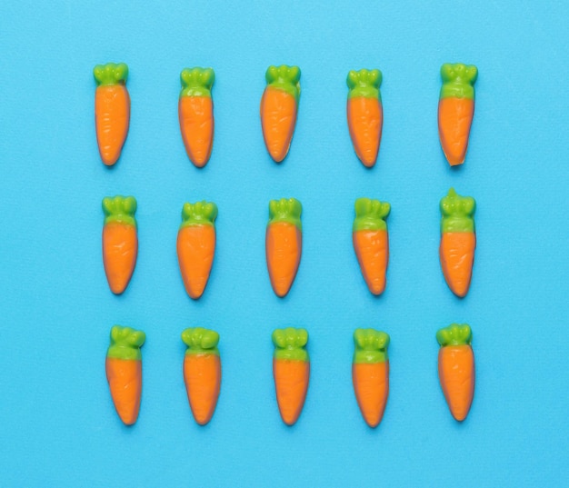 Small candy in the form of carrots stacked in three rows on a blue background Minimal harvest concept Creative photo