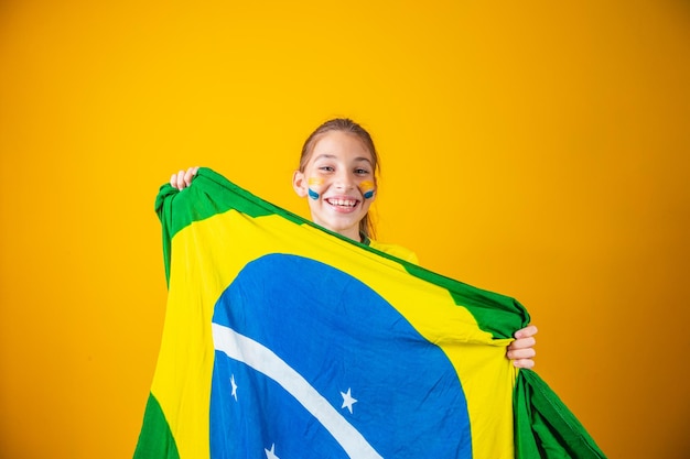 Small caucasian girl with brazil flag on yellow background. Brazilian child supporter