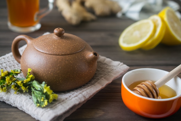 Small ceramic teapot with herbal tea on wooden table with lemon and honey